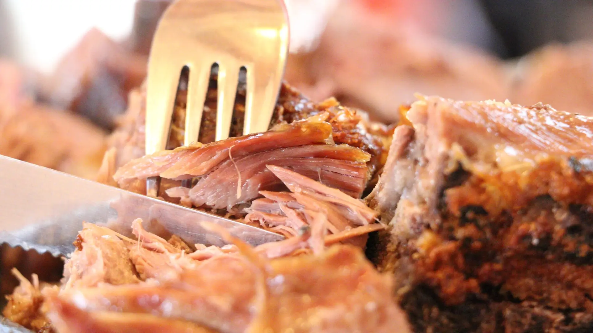 Primer plano de un tenedor y un cuchillo cortando suculenta carne asada de cordero patagónico